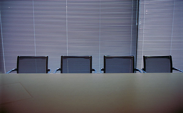 Kuva tyhjästä neuvottelupöydästä ja tuoleista hämärässä huoneessa. Kuvan lähde: Pixhill.